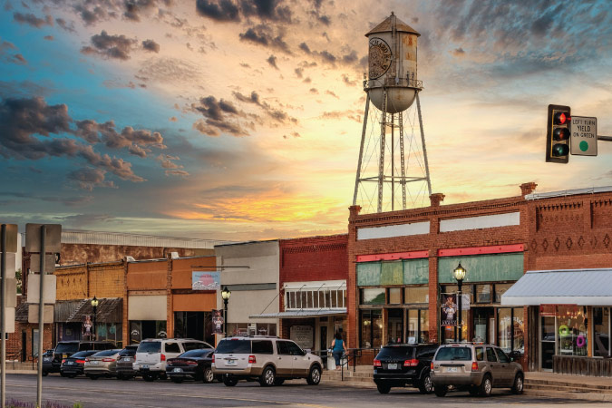 A quaint street in Blanchard, Oklahoma, at sunset, featuring a water tower in the background