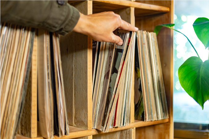 A man’s hand is selecting a record from a collection stored in direct sunlight.