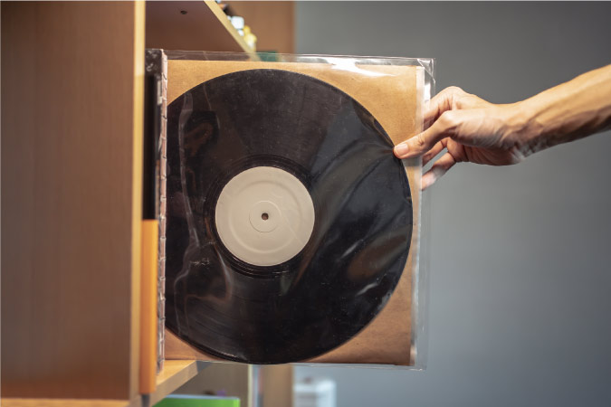 A man’s hand is pulling a well-protected vinyl record off of a shelf.