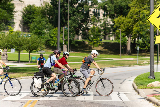 Several cyclists cross a street in the University Circle neighborhood of Cleveland, Ohio, on a sunny day.