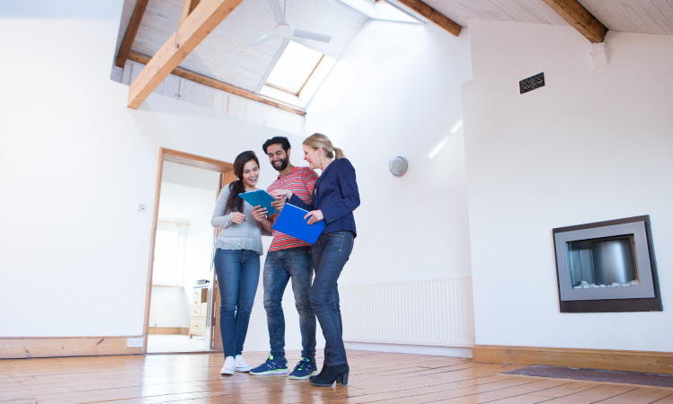 A happy couple looks over paperwork with their real estate agent while standing in the empty living room of a lovely home in Colorado Springs, Colorado.