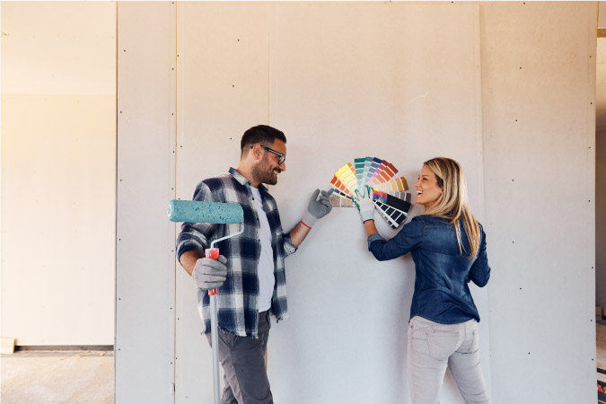 A couple is looking at paint swatches against their bare basement wall as they DIY their basement remodel.