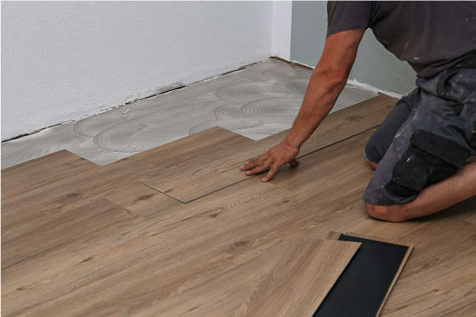 A man is installing new vinyl flooring in a basement that he is renovating. 