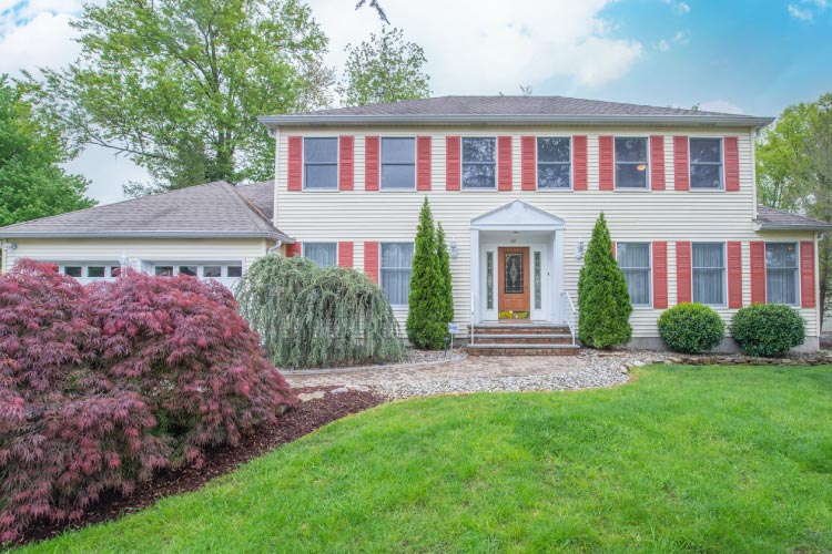 Beautiful split-level home in East Hanover Township, New Jersey. The home features a cream-colored siding exterior with nearly a dozen front-facing red-shuttered windows.