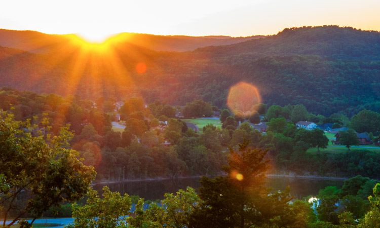 A dramatic Arkansas sunset over the Ozark Mountains' lakes in Eureka Springs. The sun's warm rays create a stunning display of colors as it sets, painting the sky with vibrant hues.