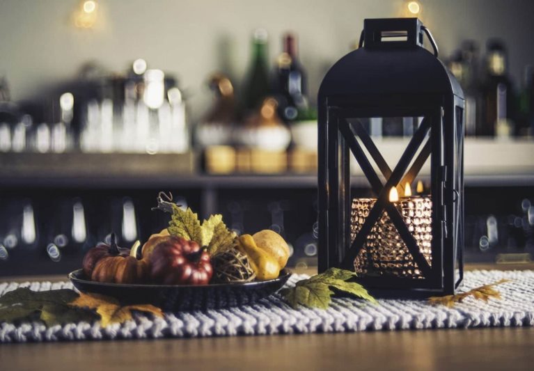 A table decorated with necessities: a candle in a lantern, decorative fall fruits, and leaves fresh from the tree