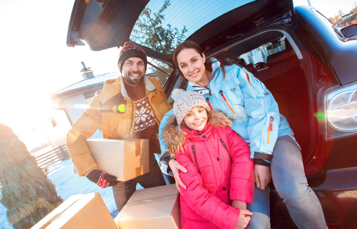 A family of three pose at the trunk of their car for a photo during their interstate move in the winter.
