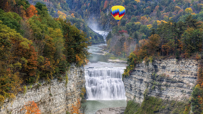 A yellow, red, and blue hot air balloon floating over Middle Falls in Finger Lakes, New York