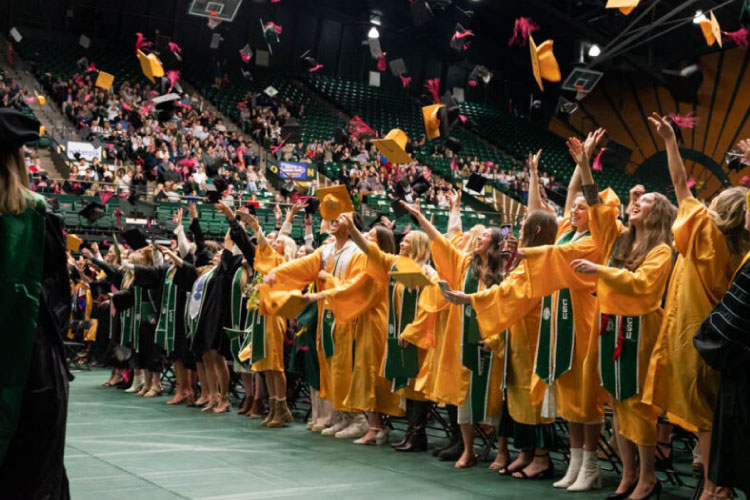 Colorado State University graduates throw their caps in the air in celebration.
