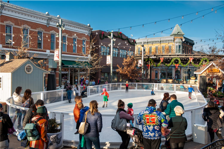 Dozens of locals are gathered around a community ice rink in Downtown Fort Collins, Colorado, on a sunny winter day.