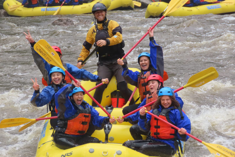 A group of friends and their river guide laugh and smile in delight as they navigate rapids while whitewater rafting on Colorado’s Cache la Poudre River.
