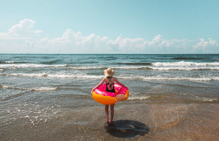 A young girl is walking into the water with an inner tube around her waist on a beach in Galveston Island, Texas.