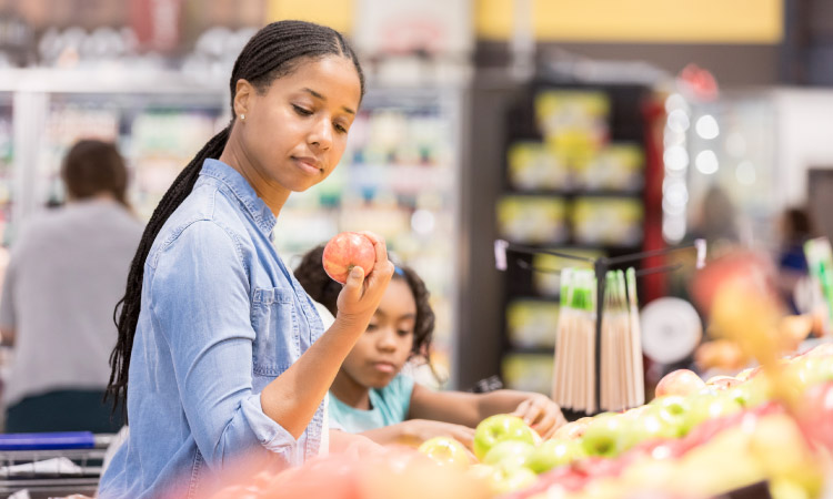 Image of a young mother and her daughter at a local grocery store, choosing apples.