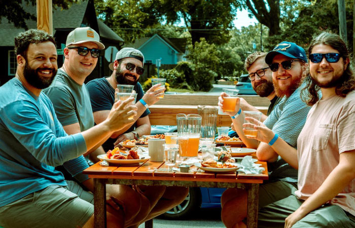 Six men smile and hold up their craft beers for a photo as they enjoy brunch at Heist Brewery in Charlotte, North Carolina.