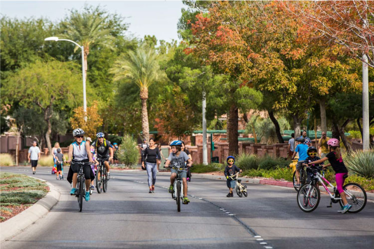 Kids and adults ride their bikes down a residential street in Henderson, Nevada, on a summer afternoon.
