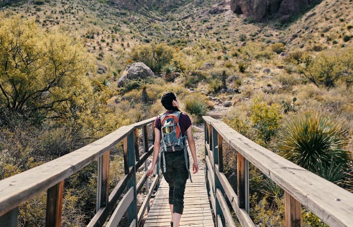 A young woman is crossing a wooden bridge while admiring the natural scenery on a hiking trail near El Paso, Texas.