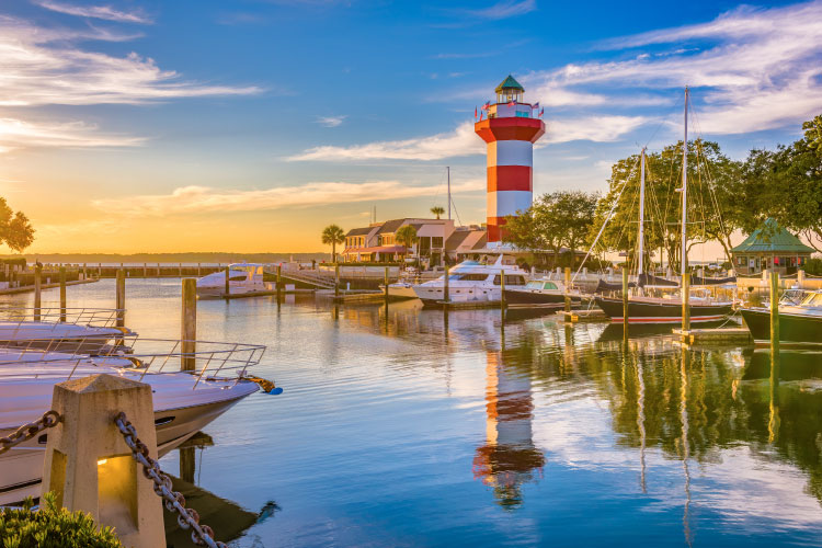 Sunrise view of the Harbour Town Lighthouse and surrounding marina on Hilton Head Island in South Carolina. The lighthouse is painted in large red and white horizontal stripes.