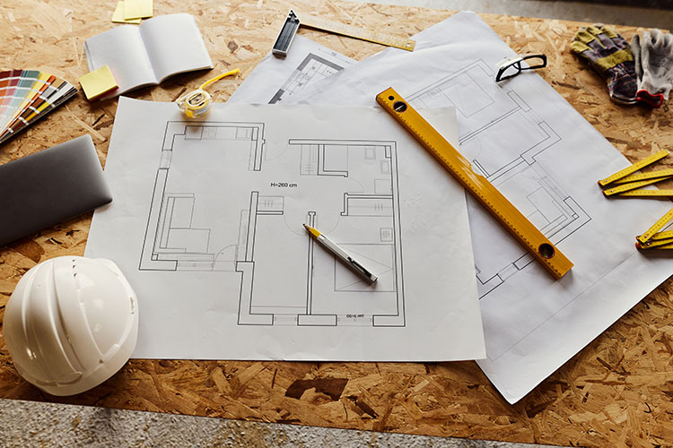 Floor plans on white paper with color samples, hard hats, rulers, and pencils