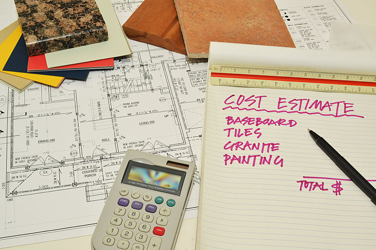 The words “Cost Estimate: Baseboard, Tiles, Granite, Painting, and Total” are written on a legal pad in pink-purple ink. The pad lies on a home’s floor plan, with a calculator and material swatches scattered about.