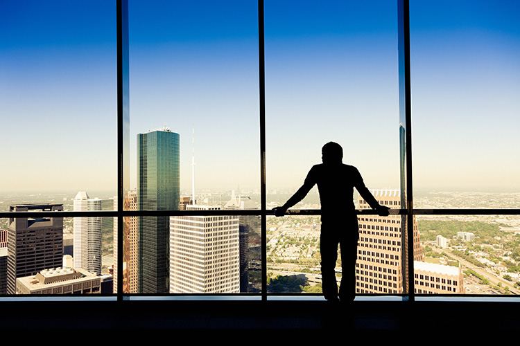 A man looks out of a high-rise office window over the city of Houston