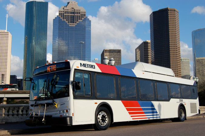A Houston METRO city bus is passing by tall city buildings as it makes its way downtown.