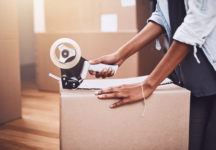 A woman tapes up a moving box in a room full of moving boxes