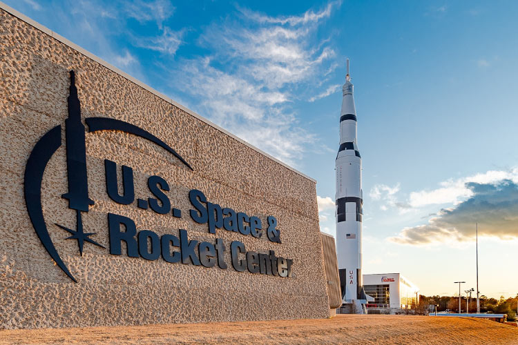 View of the large entry sign at the U.S. Space & Rocket Center in Huntsville, Alabama, with a large rocket visible in the background. 