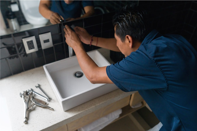 A plumber is installing a new sink and vanity during a bathroom remodel