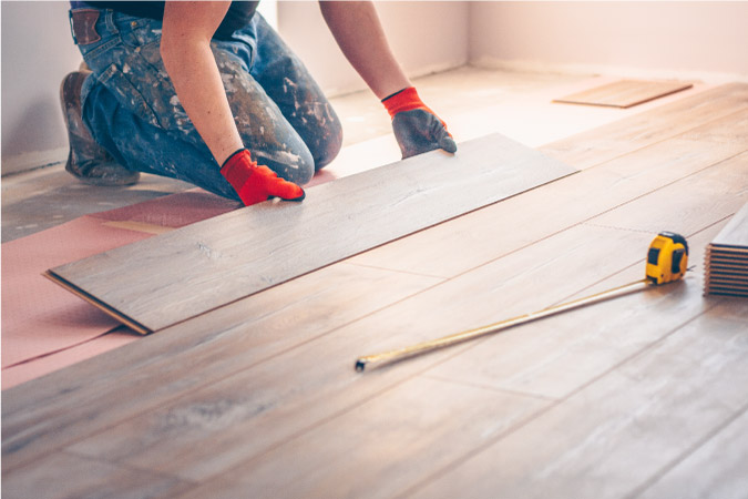 Close-up of a man installing new laminate floors, designed to look like hardwood, during a kitchen remodeling project