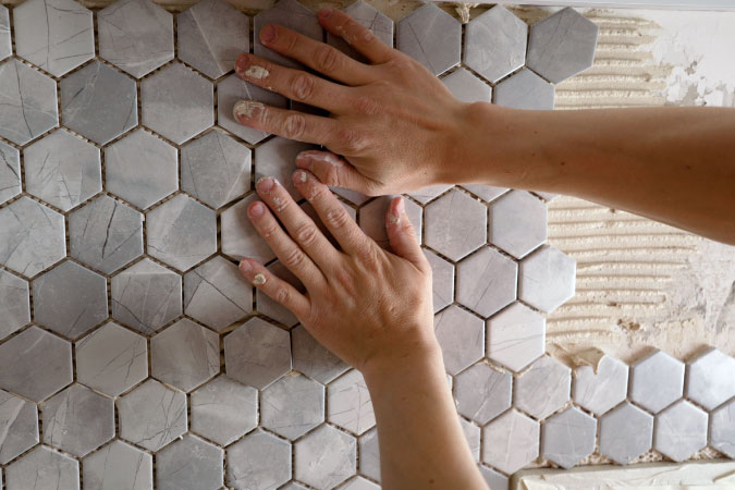 A person is using both hands to secure new tiles to a wall during a bathroom remodel