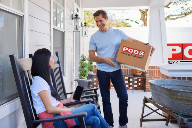 A mature couple shares a smile as the man is carrying a moving box from a PODS portable moving container into their new home in Fort Worth, Texas