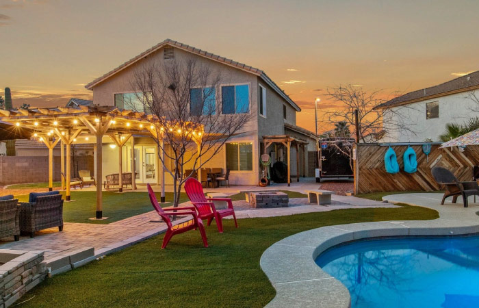 The backyard of a large single-family home in the Finley Farms neighborhood of Gilbert, Arizona. The home features a pool, large stone deck, fire pit, and green lawn.