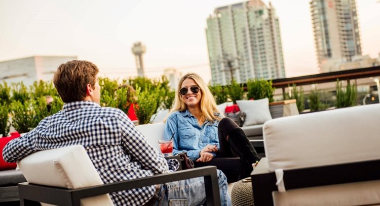  A happy couple is dining on a rooftop in downtown Dallas. Skyscrapers can be seen in the background.
