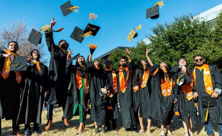 A happy group of recent graduates toss their caps in the air after graduating from University of Texas at Dallas