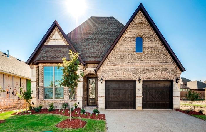 A single-family home in Dallas, TX. The home exterior features light brown brick with large wooden garage doors and a gabled roof.