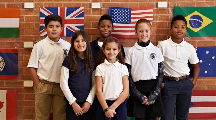 Six elementary school students are standing in front of various national flags at their school in Dallas, Texas.