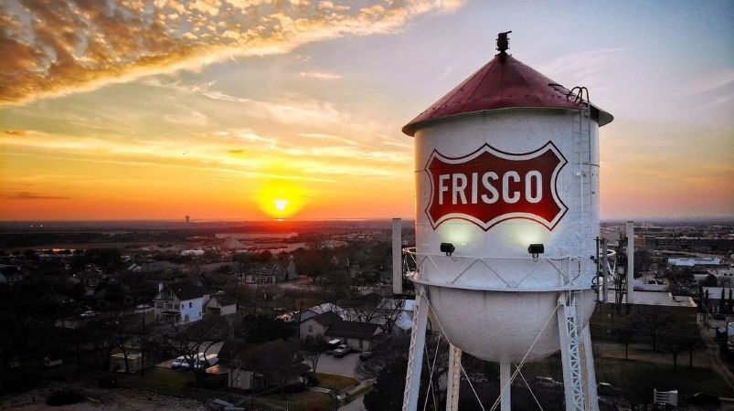 The sun is setting behind the distinct white and red water tower in Frisco, Texas.