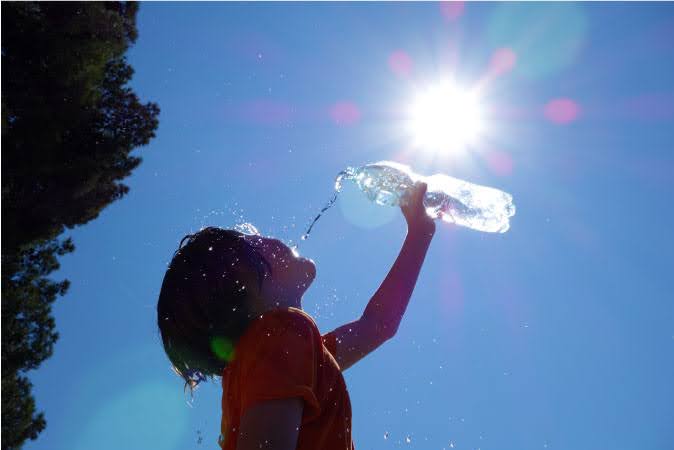A little boy is pouring water from a plastic bottle onto his face as the sun blares high above him on a hot day in Katy, Texas.