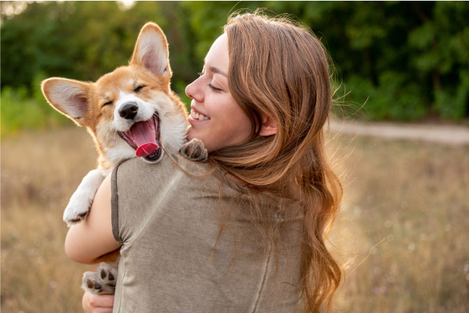 A woman is holding her corgi as it yawns happily over her shoulder.