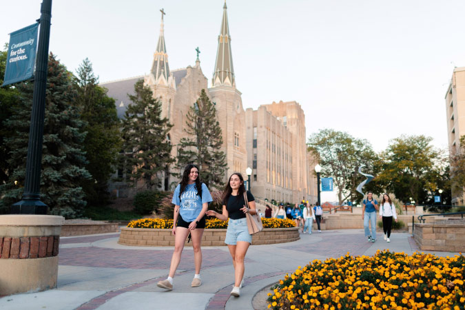 Two students walk through the campus of Creighton University in Omaha, Nebraska, with the Gothic Revival architecture of St. John’s Church visible in the background.