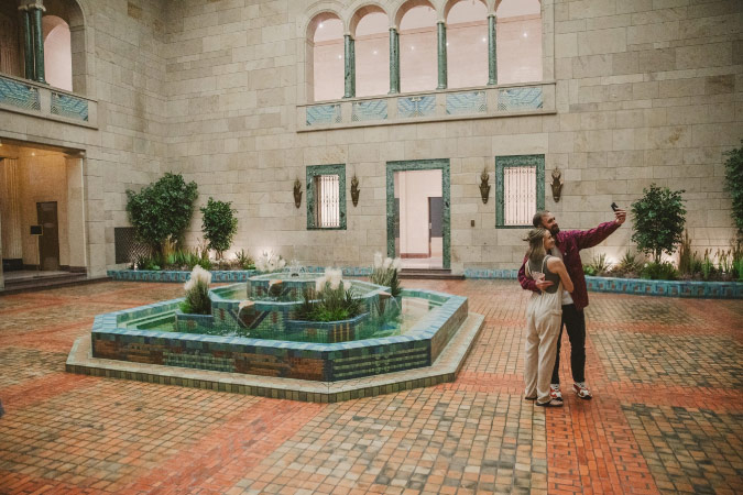 A couple takes a selfie in front of a fountain inside a gorgeous tiled courtyard at the Joslyn Art Museum in Omaha, Nebraska.