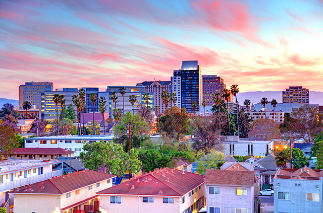 Downtown San Jose at sunset. The sky is tinged pink and blue and bathes the high-rises and townhomes in a warm, soft light.