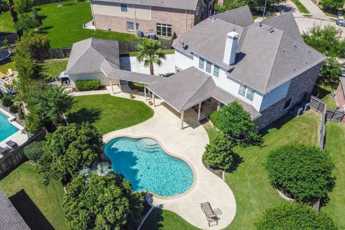Aerial view of a large two-story home with a detached garage and an inground pool in the Pine Mill Ranch neighborhood of Katy, Texas.