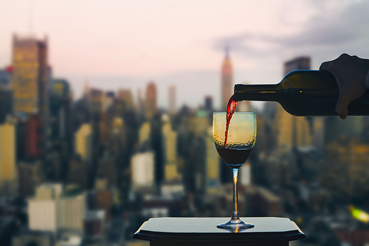 A woman pours a glass of red wine with the Manhattan skyline in the background
