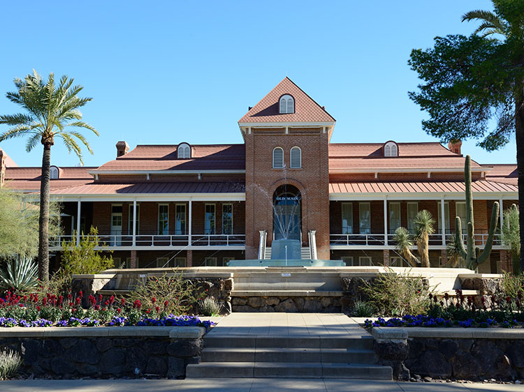 The Old Main building on the University of Arizona’s main campus. It is an old brick building with a fountain and manicured landscaping in front.