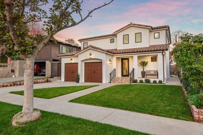 A beautiful Spanish-style home in the Alamitos Heights neighborhood of Long Beach, California, featuring two one-car garages, a tile roof, and a cleanly manicured lawn.