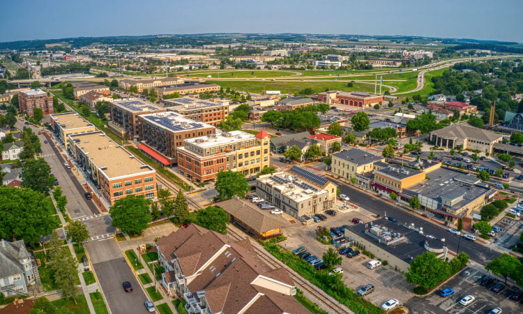 An aerial view of the Madison suburb of Middleton, Wisconsin. It’s summer and the lawns and trees in the area are lush and green. The sky is a clear blue and the buildings look bright and clean in the midday light.