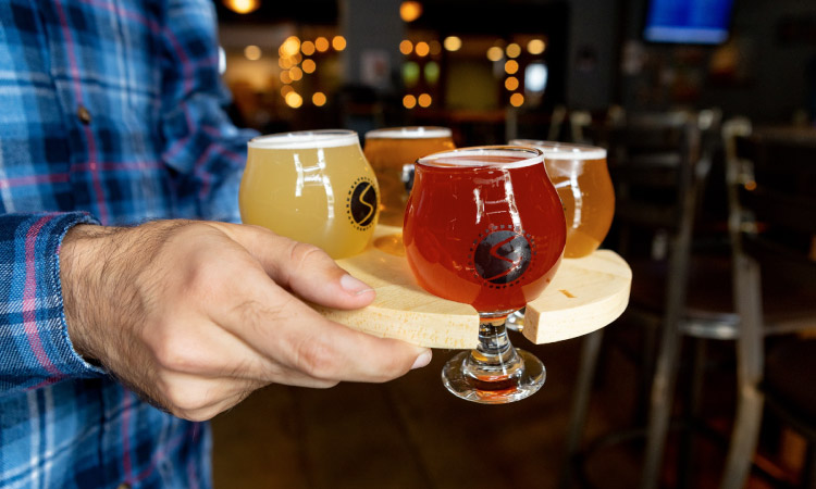 Close-up view of a man holding a flight of beers and walking them to a table at a local Madison, Wisconsin, brewery.