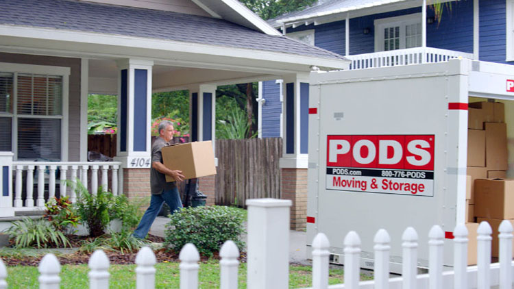 An older man is loading a PODS container in the driveway of his home