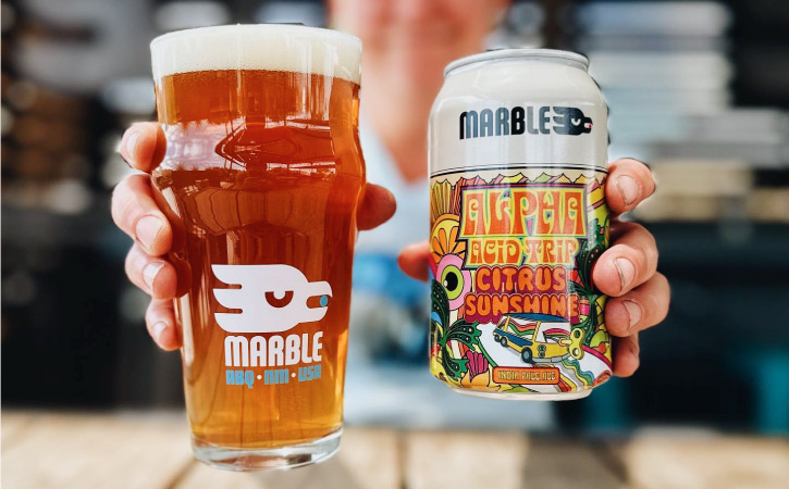 A person is holding out a freshly poured glass of craft beer and the fancy can it came from at Marble Brewery in Albuquerque, New Mexico.